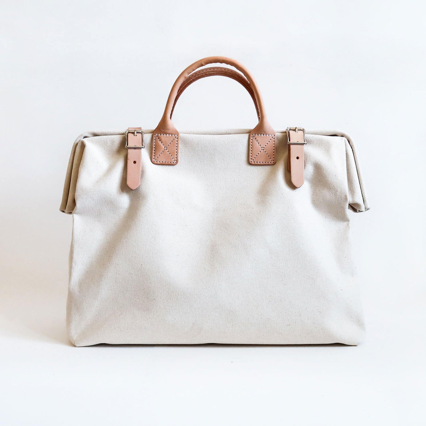 A white cotton canvas handbag with leather belted buckles with quality leather handles in between