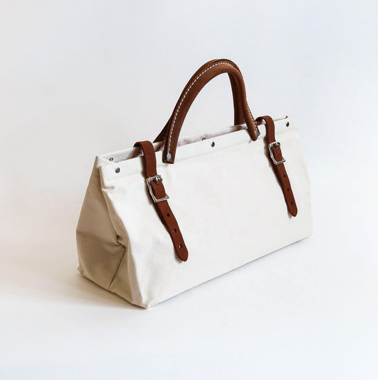 A medium sized white cotton canvas handbag with two brown suede leather belt buckle closure with a brown suede leather handle in between with white stitching