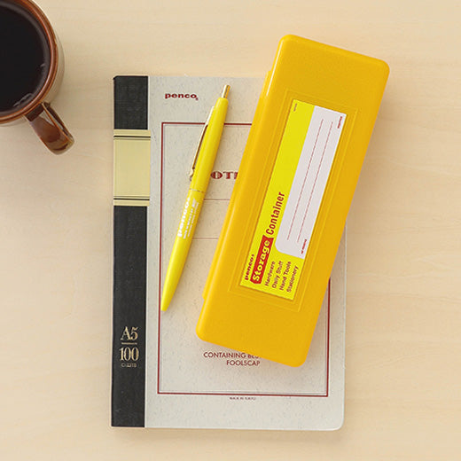 a desktop view of a yellow pen case made of plastic with write-in sticker next to a yellow ball-point pen laying on top pf a notebook that reads penco and A5